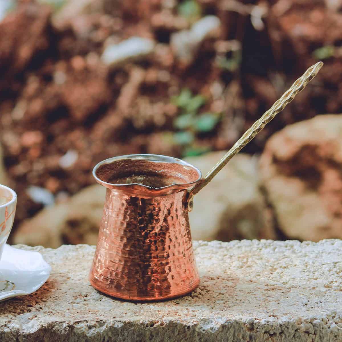 white tea cup with copper Turkish coffee pot on gray surface